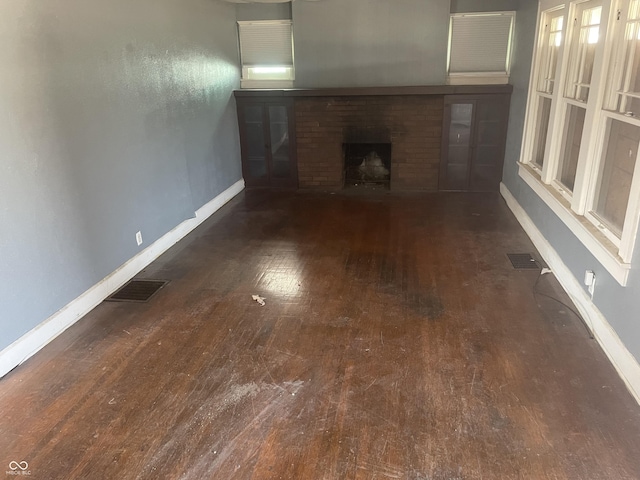 unfurnished living room with visible vents, baseboards, a brick fireplace, and hardwood / wood-style flooring