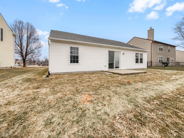 back of property with a patio, a lawn, a chimney, and a shingled roof