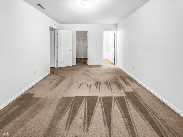 unfurnished bedroom featuring a spacious closet, visible vents, baseboards, carpet, and a closet