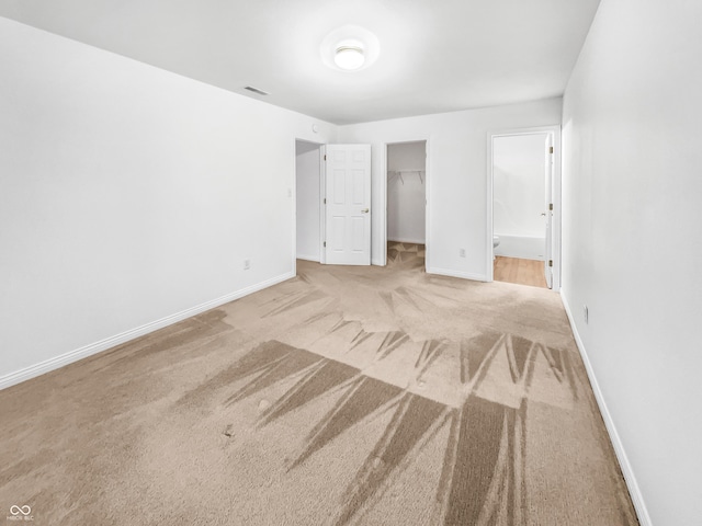 unfurnished bedroom featuring visible vents, a walk in closet, a closet, carpet, and baseboards