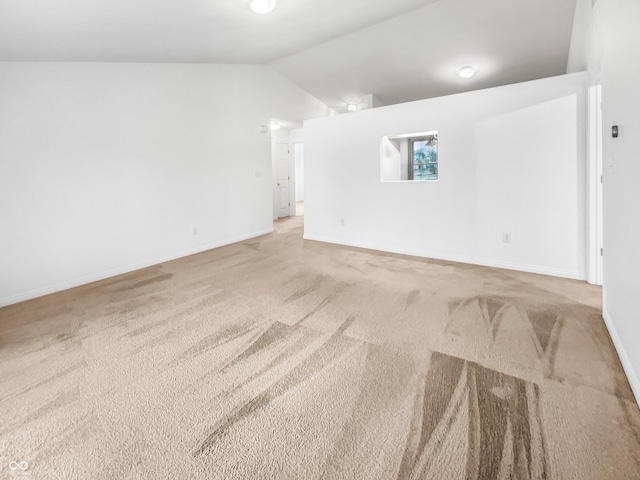 carpeted spare room featuring baseboards and vaulted ceiling