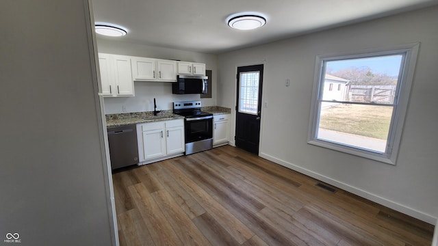 kitchen with visible vents, light stone counters, appliances with stainless steel finishes, white cabinets, and a sink