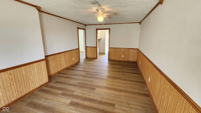 empty room with a wainscoted wall, a textured ceiling, light wood-style flooring, and wood walls