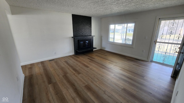 unfurnished living room with visible vents, baseboards, a fireplace, wood finished floors, and a textured ceiling