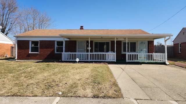 view of front facade with brick siding, a porch, a chimney, and a front yard