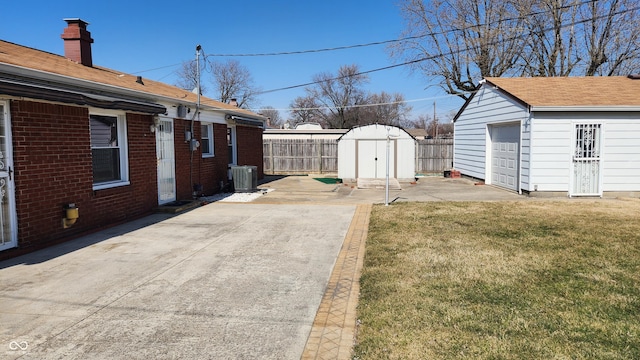 view of yard featuring a detached garage, fence, central air condition unit, a patio area, and an outbuilding