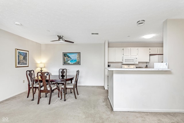 dining room with visible vents, light colored carpet, a ceiling fan, and a textured ceiling