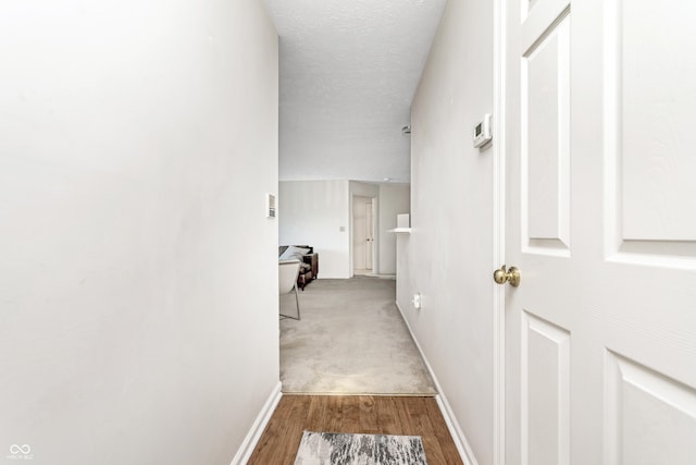 hallway featuring wood finished floors, baseboards, and a textured ceiling