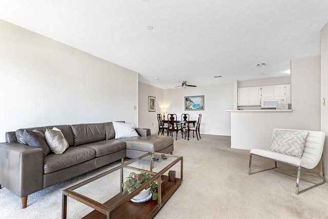 living area featuring light carpet, a textured ceiling, and ceiling fan