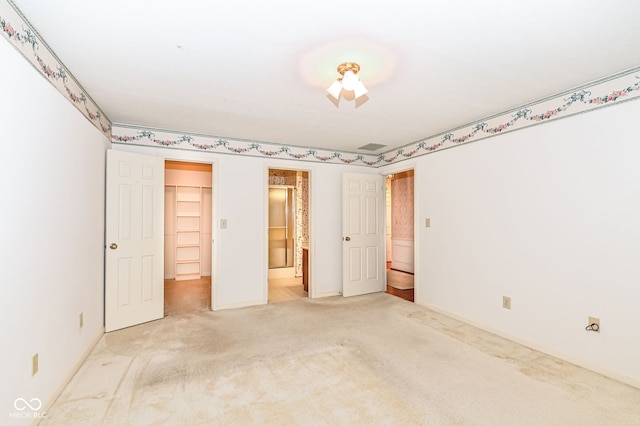 unfurnished bedroom featuring baseboards, a spacious closet, a closet, ensuite bathroom, and light carpet