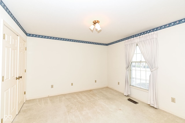 empty room featuring light colored carpet, visible vents, and baseboards