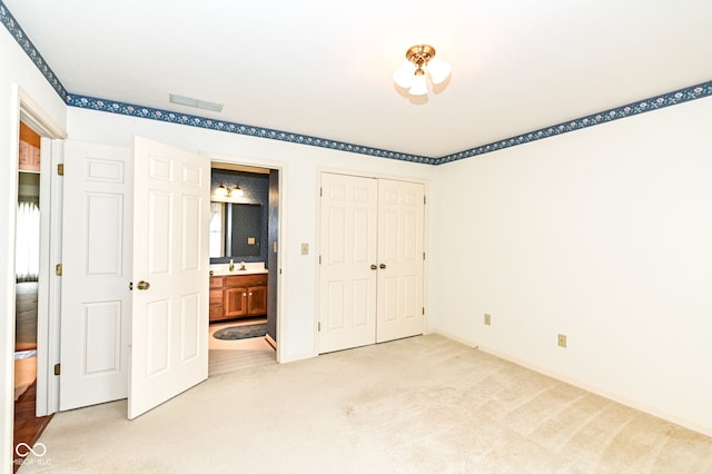 unfurnished bedroom with visible vents, light carpet, a sink, ensuite bath, and a closet