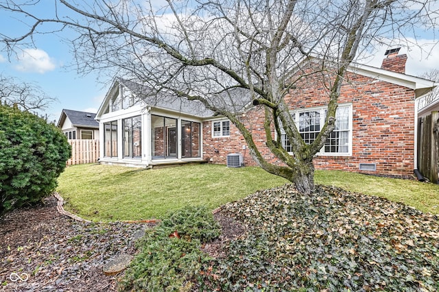 rear view of house with central AC, fence, a sunroom, brick siding, and a chimney