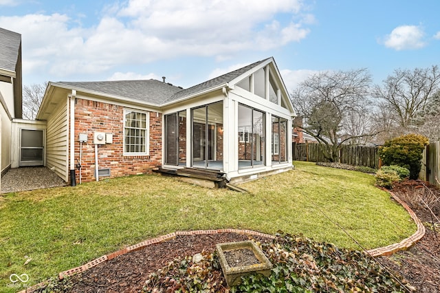 back of property featuring brick siding, roof with shingles, a lawn, a fenced backyard, and a sunroom