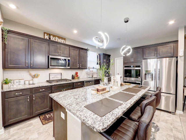 kitchen featuring a kitchen island with sink, light stone counters, stainless steel appliances, dark brown cabinets, and hanging light fixtures