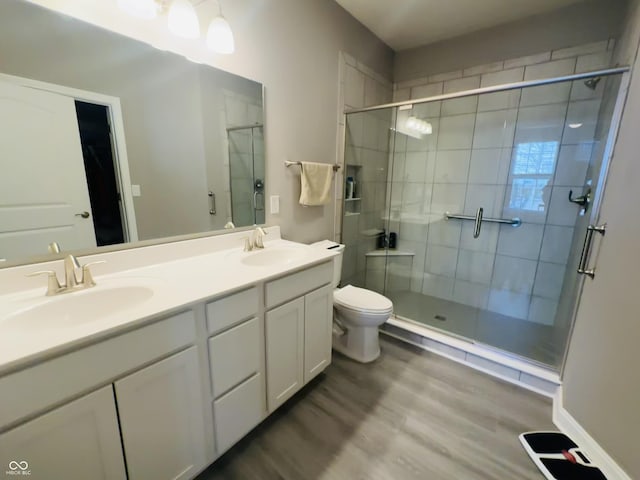 full bathroom with double vanity, wood finished floors, a stall shower, and a sink