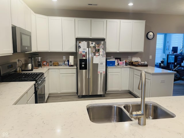 kitchen with light stone countertops, visible vents, a peninsula, a sink, and appliances with stainless steel finishes