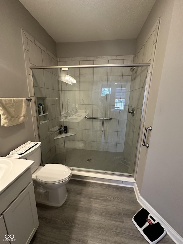 bathroom with toilet, wood finished floors, a shower stall, baseboards, and vanity