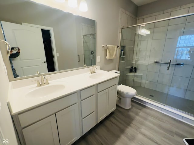 bathroom with a shower stall, wood finished floors, double vanity, and a sink