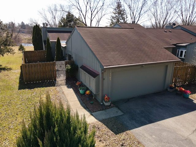 exterior space with fence, a yard, a shingled roof, a garage, and aphalt driveway