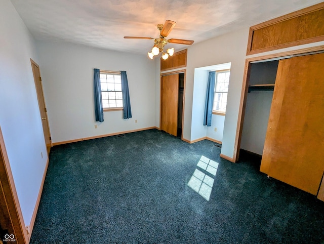 unfurnished bedroom featuring a ceiling fan, baseboards, multiple closets, and dark carpet