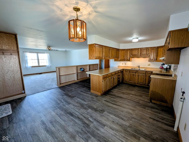 kitchen featuring a sink, dark wood finished floors, a peninsula, brown cabinetry, and light countertops