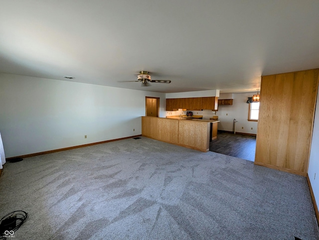 unfurnished living room featuring ceiling fan, baseboards, and dark colored carpet