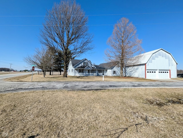 view of front facade with covered porch, a gambrel roof, driveway, and a detached garage