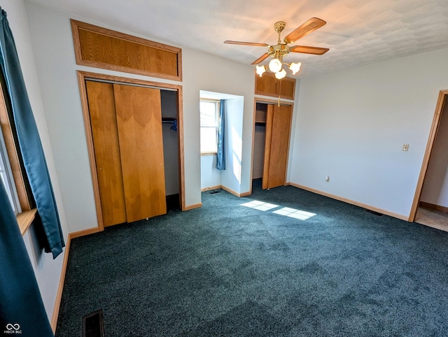 unfurnished bedroom with baseboards, multiple closets, visible vents, and dark carpet