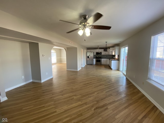 unfurnished living room featuring dark wood finished floors, a ceiling fan, arched walkways, and a wealth of natural light