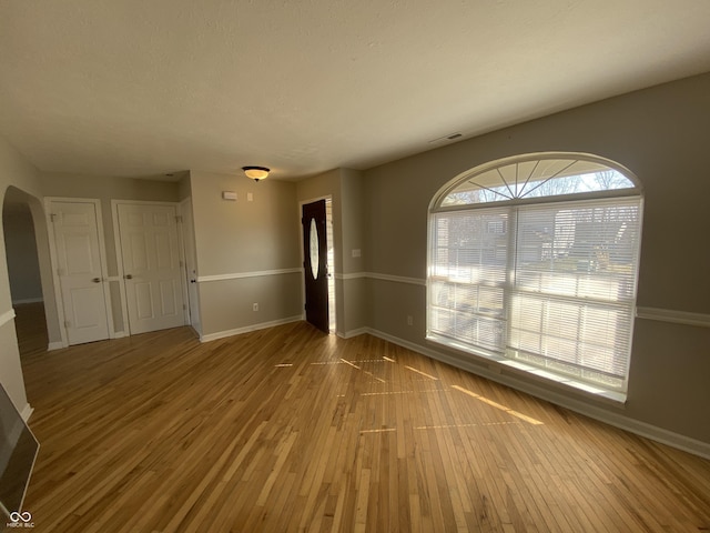 empty room with hardwood / wood-style floors, visible vents, baseboards, and arched walkways