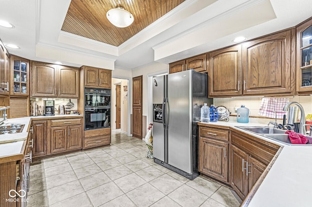 kitchen featuring light countertops, a tray ceiling, stainless steel fridge, dobule oven black, and a sink