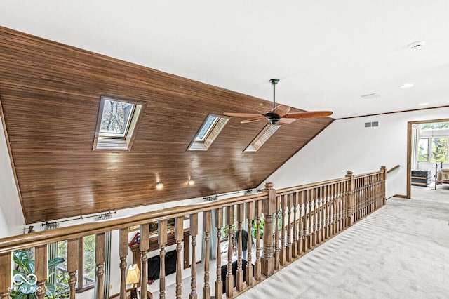 hallway with lofted ceiling with skylight, visible vents, carpet flooring, and an upstairs landing