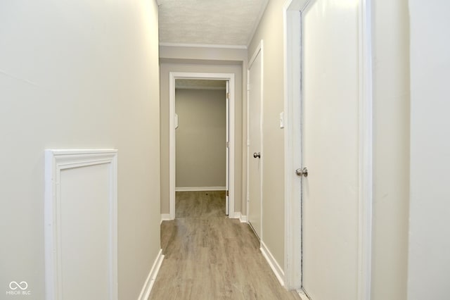 hall featuring baseboards, a textured ceiling, and light wood-style floors