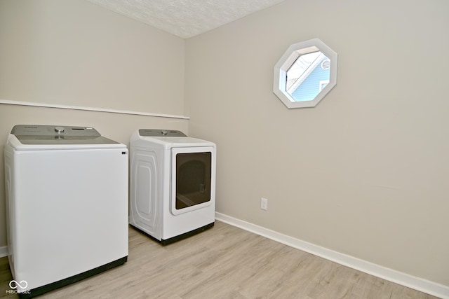 laundry room with a textured ceiling, light wood finished floors, baseboards, laundry area, and washing machine and clothes dryer