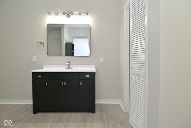 bathroom with a closet, vanity, baseboards, and wood finished floors