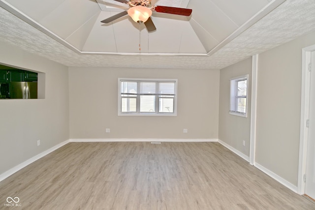 unfurnished room with a ceiling fan, baseboards, vaulted ceiling, a textured ceiling, and light wood-type flooring