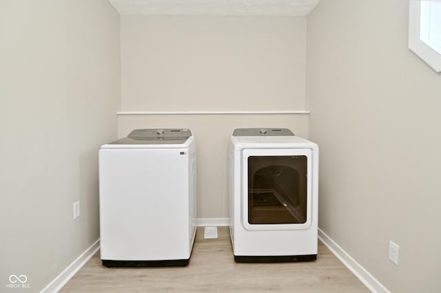 laundry area with light wood-type flooring, baseboards, laundry area, and washer and clothes dryer