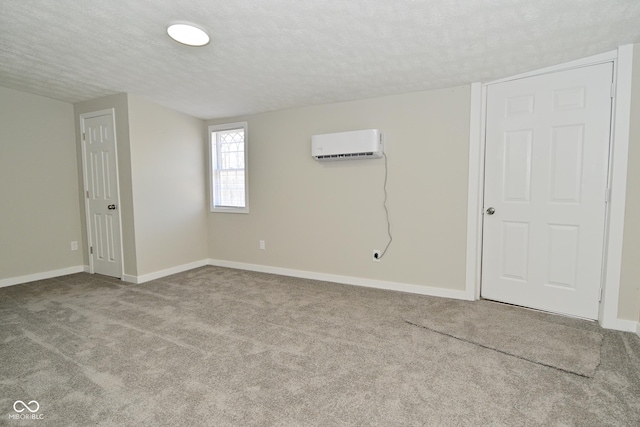 spare room with a wall mounted air conditioner, baseboards, carpet floors, and a textured ceiling