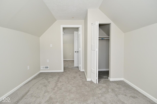 unfurnished bedroom featuring baseboards, visible vents, vaulted ceiling, a textured ceiling, and carpet flooring