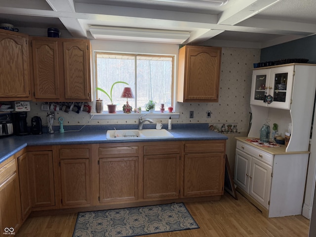 kitchen featuring beamed ceiling, wallpapered walls, light wood-type flooring, and a sink