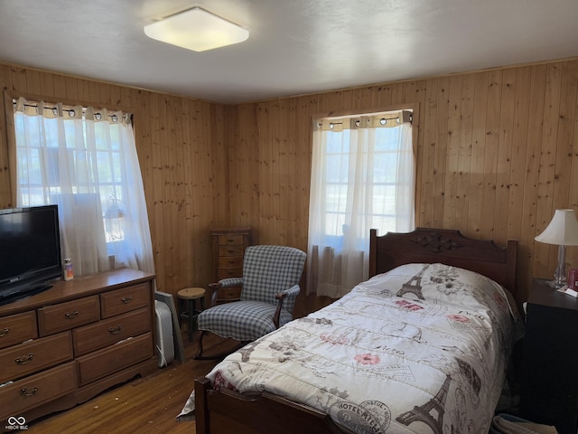 bedroom with multiple windows, wood finished floors, and wood walls