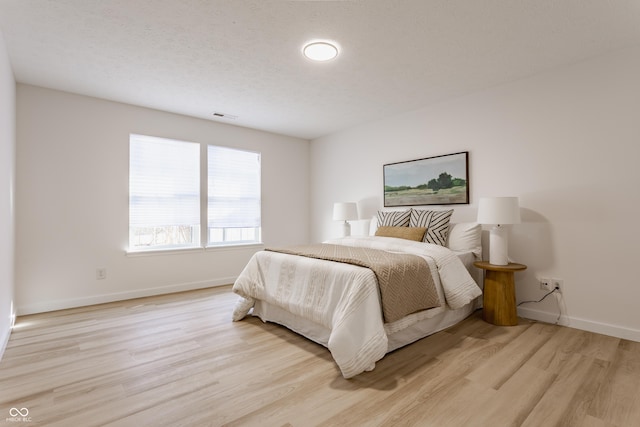 bedroom with light wood finished floors, visible vents, a textured ceiling, and baseboards