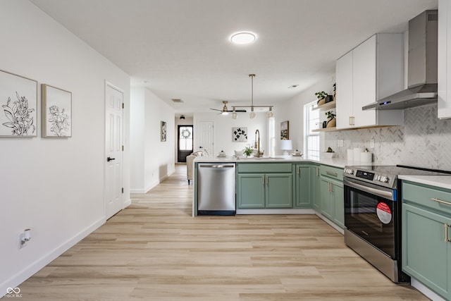 kitchen featuring a peninsula, wall chimney exhaust hood, stainless steel appliances, and green cabinetry