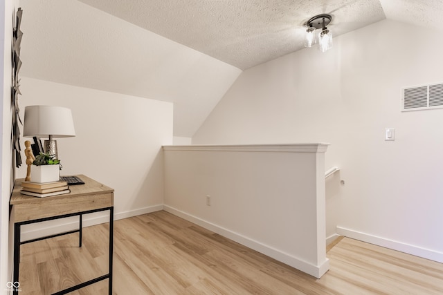 interior space featuring lofted ceiling, visible vents, light wood-type flooring, and a textured ceiling