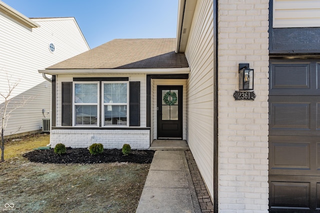 property entrance featuring brick siding and a shingled roof