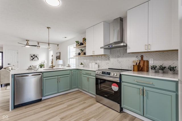 kitchen featuring a sink, wall chimney range hood, a peninsula, stainless steel appliances, and open shelves