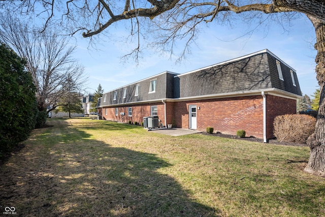 back of property with mansard roof, a shingled roof, central air condition unit, a lawn, and brick siding