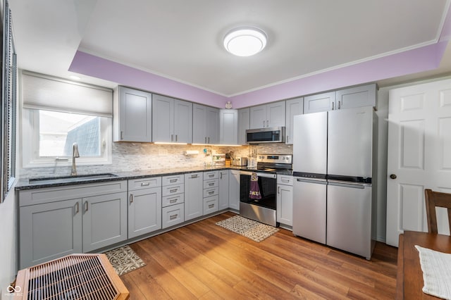 kitchen featuring gray cabinetry, decorative backsplash, light wood-style flooring, appliances with stainless steel finishes, and a sink