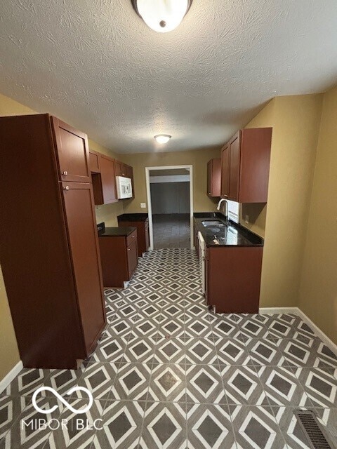 3302 E 42nd St, Indianapolis, IN 46205 - kitchen with dark countertops, white microwave, baseboards, and a sink